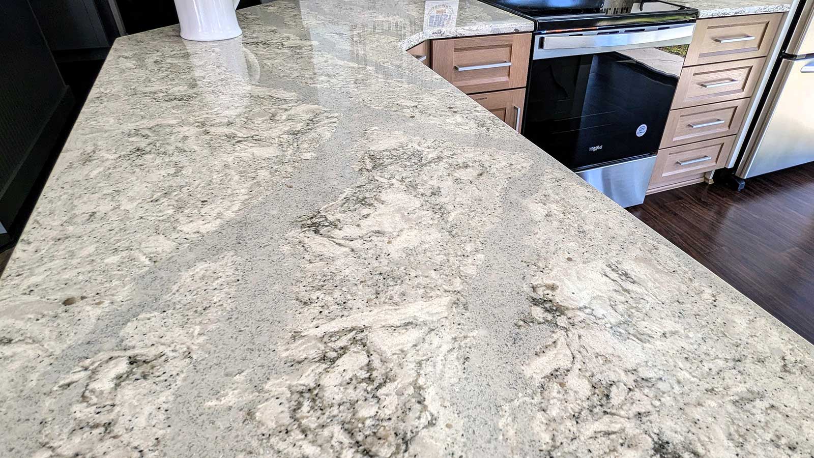 Close-up of a kitchen with light grey granite countertops featuring intricate patterns. Wooden cabinets and stainless steel appliances are visible in the background, adding a modern touch to the space.