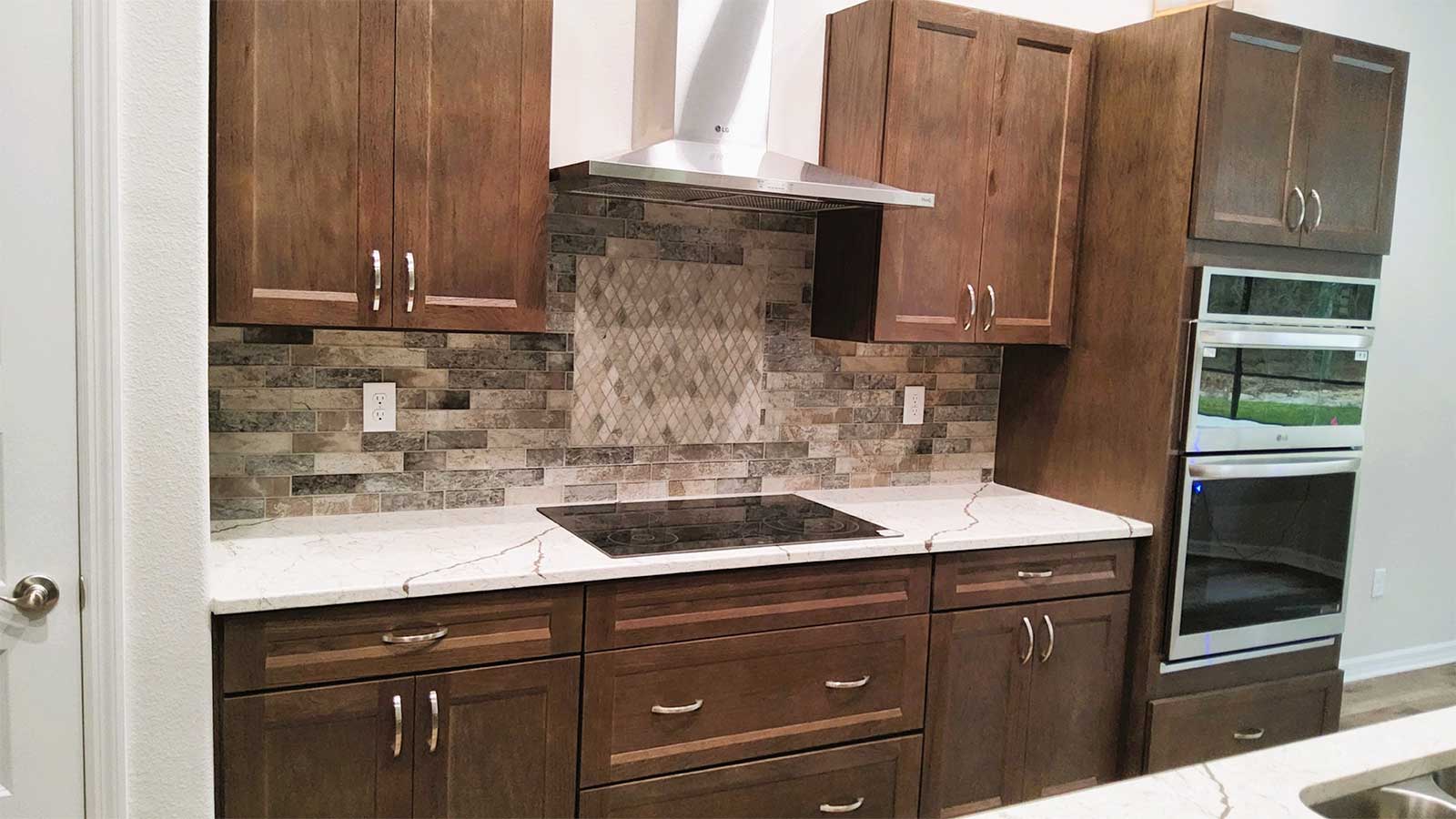 Sweetwater-Homes Modern kitchen with wooden cabinets, a stainless steel range hood, an electric cooktop, stone tile backsplash, marble countertops, and a built-in double wall oven.